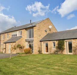 A stone farmhouse with multiple windows and doors surrounded by a lawn at Fontburn Farmhouse Ewesley near Rothbury
