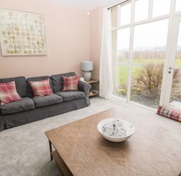 A living room with a gray sofa and plaid cushions a wooden coffee table and large windows at Fontburn Farmhouse in Ewesley near Rothbury