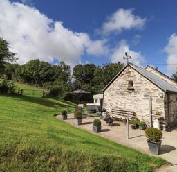 A stone house with a patio area and garden furniture on a grassy hillside at Y Felin at Coed Cadw in Felindre Farchog near Newport Pembrokeshire