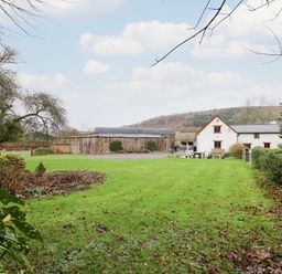 A green lawn with a white house and wooden barn in the background at Maes Y Berllan Barn in Gilwern