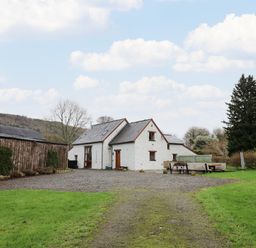 A white stone house with a slate roof next to a wooden barn and a gravel driveway at Maes Y Berllan Barn in Gilwern