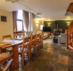 A dining area with a wooden table and chairs and a living area with sofas a wood stove and a carved wooden dragon at Maes Y Berllan Barn in Gilwern