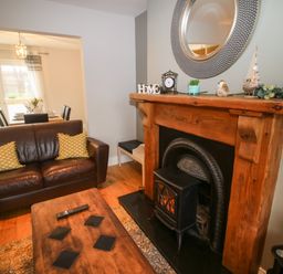 A living room with a brown leather sofa a wooden coffee table and a fireplace with decorations at Pebble Lodge in Kenmare County Kerry