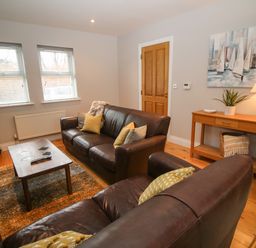 A living room with brown leather sofas, coffee table, rug, wooden side table with lamp and plant and a painting on the wall at Pebble Lodge in Kenmare County Kerry