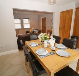 A dining area with a wooden table set with dishes and flowers with a living room with sofas in the background at Pebble Lodge in Kenmare County Kerry
