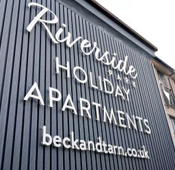 A sign on a building reading Riverside Park Holiday Apartments and beckandtarn.co.uk at Riverside Park in Keswick
