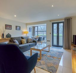 A living room with two blue chairs a gray sofa a wooden coffee table a dining table with chairs and a TV on a wooden stand at Riverside Park 2 in Keswick