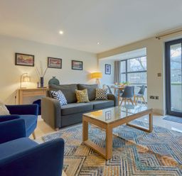 A living room with blue armchairs gray sofa wooden coffee table and dining area by a window at Riverside Park 2 in Keswick