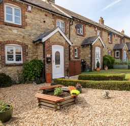 A stone cottage with white doors surrounded by a gravel garden and wooden planter at Knapp Cottage in Chickerell