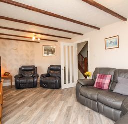 A living room with leather sofas a wooden TV stand a flat screen TV and pictures on the walls at Knapp Cottage in Chickerell