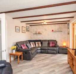 A living room with a leather corner sofa cushions wooden side table wall shelves wall clock and wooden TV stand at Knapp Cottage in Chickerell