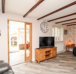 A living room with a wooden TV stand holding a television a large wall clock leather armchairs and a wooden side table with a lamp at Knapp Cottage in Chickerell