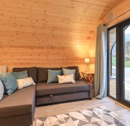 A living room with a gray sofa with cushions a side table with a lamp and glass doors at Jenny - Crossgate Luxury Glamping in Hartsop near Glenridding