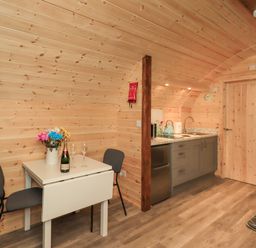 A wooden interior with a small dining table with two chairs and a kitchenette with grey cabinets and a sink at Jenny - Crossgate Luxury Glamping in Hartsop near Glenridding