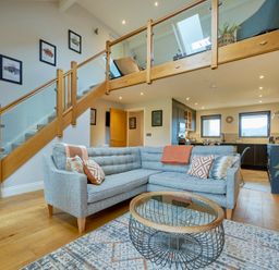 An open-plan living room and kitchen with a grey sectional sofa and glass coffee table at Riverside Park 6 in Keswick