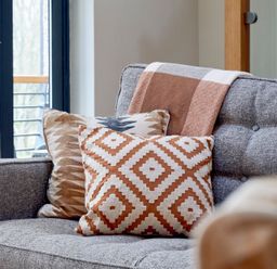 A gray fabric sofa with patterned cushions and a blanket near a window at Riverside Park 6 in Keswick