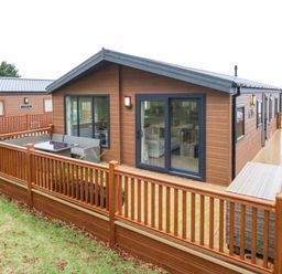 A wooden cabin with a fenced deck and outdoor seating in a grassy area at Woodpecker Lodge in Dunbar