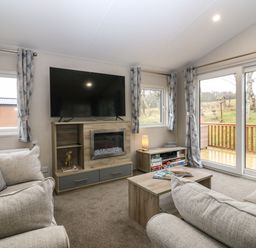 A living room with sofas a wall-mounted television a fireplace a coffee table and sliding glass doors at Woodpecker Lodge in Dunbar