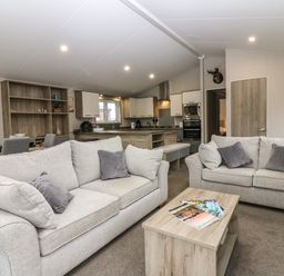 A living room with two sofas and a wooden coffee table with magazines and a kitchen with cabinets and appliances at Woodpecker Lodge in Dunbar