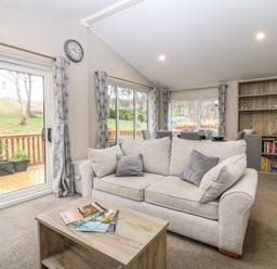 A living room with a beige sofa and a wooden coffee table with magazines at Woodpecker Lodge in Dunbar
