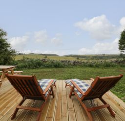 Two wooden lounge chairs with cushions on a deck facing a grassy yard and fields beyond at Lime Kiln in Blagdon