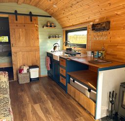 A compact kitchen with wooden cabinets and a small stove next to a bedroom with a sliding wooden door at Lime Kiln in Blagdon