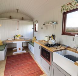 A kitchen and dining area with wooden countertops a gas stove a sink a small dining table with two cushioned benches and a red rug at Balwen Shepherd's Hut in Berriew