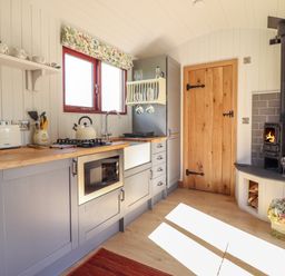 A kitchen with wood countertops a stove toaster and a wood burning stove near a wooden door at Balwen Shepherd's Hut in Berriew