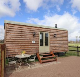 A wooden shepherd's hut with stairs leading to double doors and a metal table with two chairs outside in a field at Balwen Shepherd's Hut in Berriew