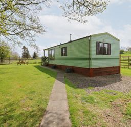 A green mobile home with a pathway leading to it and a picnic table in a grassy yard at Row End farm in Brough