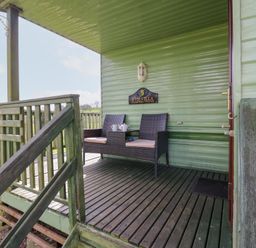 A porch with wooden railing and two chairs with a small table at Row End farm in Brough