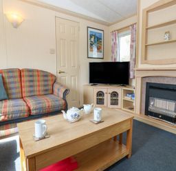 A living room with a checkered sofa a wooden coffee table with teapot and mugs a television and a fireplace at Row End farm in Brough