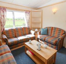 A sitting room with patterned sofas a wooden coffee table with mugs and teapot and windows showing a green field at Row End farm in Brough