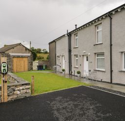 A row of houses with front doors and windows overlooking a lawn and a driveway with a charging station at Oxen Park Farm Cottage Oxen Park near Ulverston