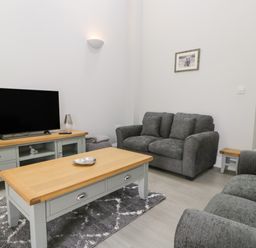 A living room with a television on a wooden cabinet a coffee table and grey sofas at Bill's Barn in Oxen Park near Ulverston