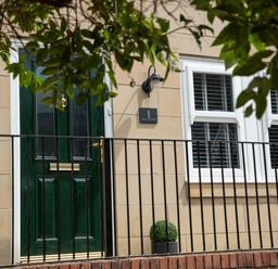 A green door next to two white windows with black railing and a small plant at 1 Wesley Mews in Alnwick