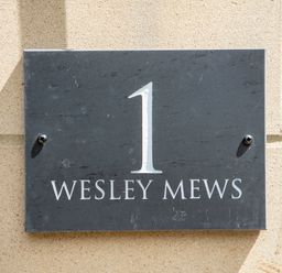 A black house number plaque with number 1 and text Wesley Mews on a beige brick wall at 1 Wesley Mews in Alnwick