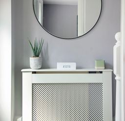 A radiator cover with a potted plant a keys box and a small container beneath a round wall mirror at 1 Wesley Mews in Alnwick