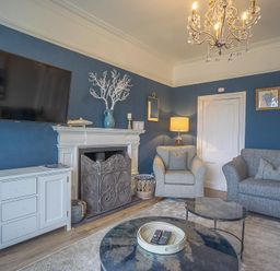 A living room with a grey sofa and armchair a white fireplace and a wall mounted TV at Argoed in Abersoch