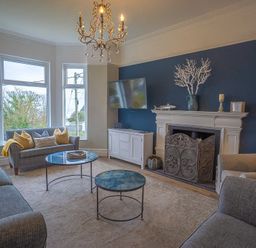 A living room with sofas a fireplace a mounted TV and large windows at Argoed in Abersoch