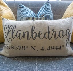 A sofa with grey checkered fabric and pillows including one with Llanbedrog and coordinates printed on it at Argoed in Abersoch
