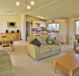 A living room and kitchen area with green sofas a wooden coffee table dining table and chairs at Arwelfa Lodge in Abersoch