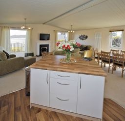 An open living and dining area with a kitchen island a sofa a dining table and windows at Arwelfa Lodge in Abersoch