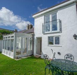 A white two-story house with a glass conservatory and a metal outdoor table and chairs on a lawn at Bryn Awel in Mynytho near Abersoch