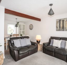 A living room with two brown leather sofas and cushions a lamp on a small table and a dining table visible in the background at Bywyd Da 232 Cae Du Abersoch