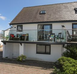 A house with a balcony with glass railing and outdoor furniture in front of a garage at Bywyd Da 232 Cae Du in Abersoch