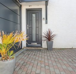 A front door with two potted plants on a brick driveway at Bywyd Da 232 Cae Du in Abersoch