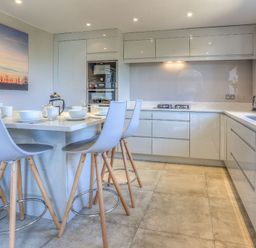 A modern kitchen with a dining island with chairs and white cabinets at Cromlin Glas in Abersoch