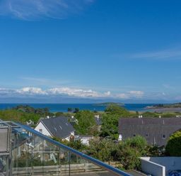 A view of houses trees and the sea with an island in the background at Cromlin Glas in Abersoch