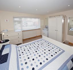 A bedroom with a bed covered in a blue and white polka dot quilt next to a dresser and wardrobe at Eleri in Abersoch